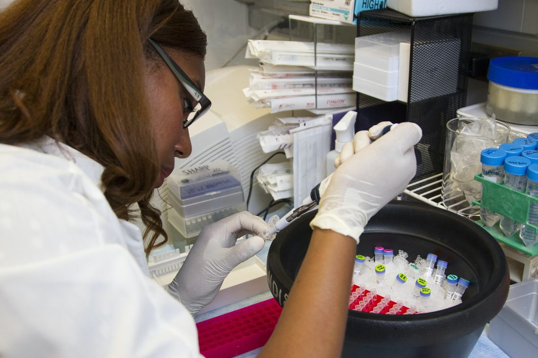 A laboratory scientist pipetting a sample into a vial on ice at a testing bench.