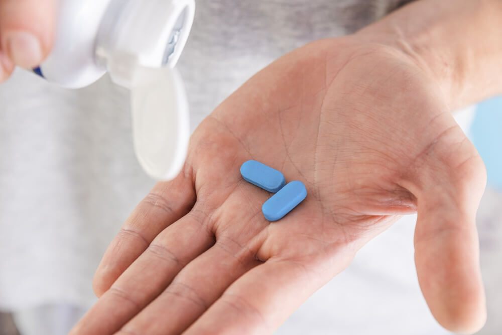An open palm holding two blue tablets, with a pill bottle tipped over it.